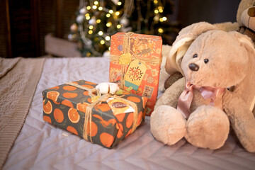 A New Year's card, a teddy bear sitting next to New Year's gifts, on the background of a Christmas tree