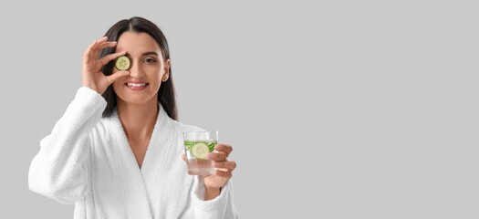 Wall Mural - Beautiful woman holding glass of cucumber infused water on grey background with space for text