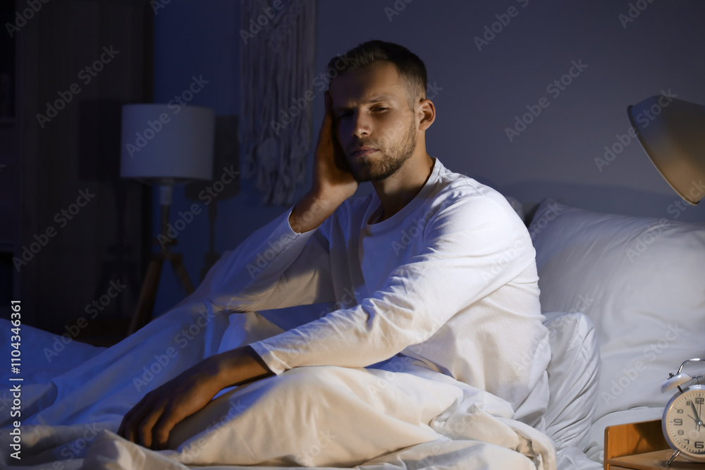 Young man suffering from insomnia on bed in bedroom at late night