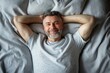 © Pete - Smiling man relaxes in bed. Top view photo shows happy middle-aged European man laying in comfy bed. Enjoys morning. Man hands behind head. Comfy bedding, peaceful atmosphere. Perfect for relaxation,