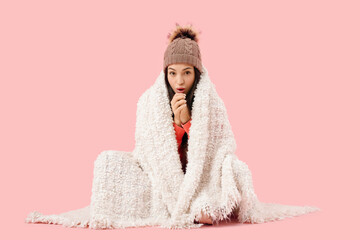 Wall Mural - Frozen young woman in hat with warm plaid sitting on pink background