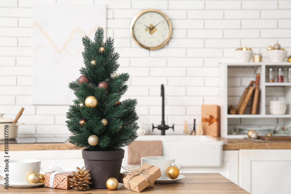 Small Christmas tree with balls, presents and coffee cup on table in kitchen