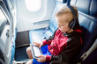 © Brocreative - A young boy airplane passenger is busy playing and watching his tablet computer while on a long flight. Child staying busy in front of a screen while traveling.