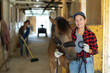 © JackF - Female leads horse by bridle, takes animal out of stall and follows it to place of training and walking. Female owner of animal pulls animal behind her, leads her to racetrack.