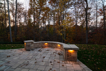 Wall Mural - a cozy stone patio illuminated by warm lights during twilight, surrounded by an autumn forest and sc