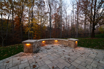 Wall Mural - a cozy stone patio illuminated by warm lights during twilight, surrounded by an autumn forest and sc