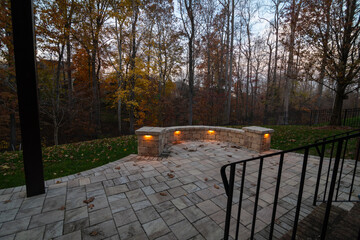 Wall Mural - a cozy stone patio illuminated by warm lights during twilight, surrounded by an autumn forest and sc