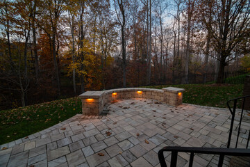 Wall Mural - a cozy stone patio illuminated by warm lights during twilight, surrounded by an autumn forest and sc