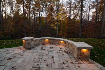 Wall Mural - a cozy stone patio illuminated by warm lights during twilight, surrounded by an autumn forest and sc