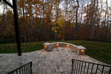 Wall Mural - a cozy stone patio illuminated by warm lights during twilight, surrounded by an autumn forest and sc