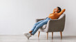 © Prostock-studio - Gorgeous Asian woman sitting in comfy armchair, being lazy, feeling peaceful against white studio wall, panorama with copy space. Attractive young lady resting and relaxing with hands behind head