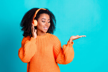 Wall Mural - Photo of pretty young girl earphones hold look empty space wear trendy knitwear orange outfit isolated on aquamarine color background