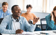 © Prostock-studio - Learning Concept. Portrait of interested African American guy sitting at table with multi ethnic classmates, talking to teacher, asking or answering question, discussing new theme, topic or theory
