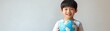 © Thanaseth - Asian boy holding a globe, standing against a clean white backdrop, symbolizing the world of opportunities and international understanding