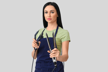 Wall Mural - Female hairdresser with iron and tongs for hair extension on light background