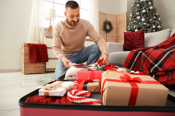 Sticker - Young man packing suitcase on floor in living room. Christmas travel concept