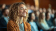 © Keopaserth - smiling woman with curly hair enjoys presentation in crowded auditorium, radiating positivity and engagement