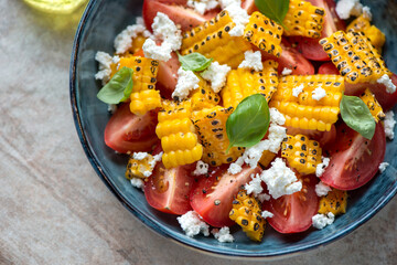 Wall Mural - Close-up of salad with red tomatoes, grilled corn and cheese served in a blue bowl, horizontal shot