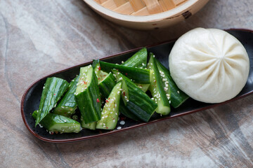 Wall Mural - Plate with chinese smashed cucumber salad and steamed bao, horizontal shot on a brown granite background, selective focus