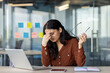 © Liubomir - Hispanic woman businesswoman experiencing stress at work, holding glasses in hand, sitting in front of laptop and phone. Expression reflects work pressure and decision-making challenges.
