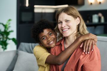 Wall Mural - Smiling woman being hugged by child with bright expression while sitting on a couch in a modern living room setting