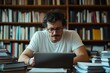 © c80 - A man wearing glasses intensely focuses on a laptop in a library, surrounded by stacked books, conveying a dedicated study or work environment.