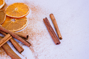 A pile of orange slices and cinnamon sticks on a white background. The oranges are cut in half and the cinnamon sticks are whole. Concept of warmth and comfort