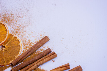 A pile of orange slices and cinnamon sticks on a white background. The oranges are cut in half and the cinnamon sticks are whole. Concept of warmth and comfort