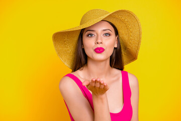 Canvas Print - Close up portrait of girl in a brimmed hat sends an air kiss from her palm looking straight into the camera isolated on yellow background