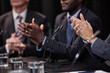 © Seventyfour - Cropped shot of female politician applauding in support of colleagues speech while sitting around meeting table with diverse team of officials in conference room