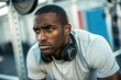 © SerPak - A man is intently focusing on his workout in a gym setting. He is wearing a light t shirt and headphones as he prepares to lift weights. The gym has various equipment in the background, illustrating a