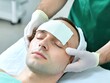 © Sumet - Male Patient Receiving Facial Treatment with Bandage on Forehead in Medical Spa Environment by Dermatologist in Green Scrubs