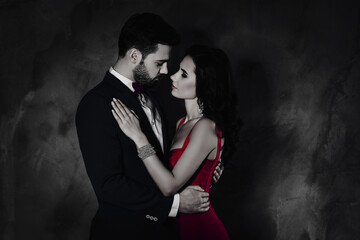 Poster - Side view portrait of attractive lovely couple, virile harsh gentleman in tuxedo embracing his pretty charming lady on waist looking at each other face to face isolated on grey background