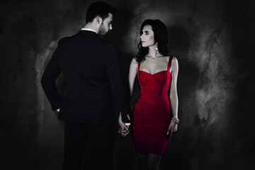 Aufkleber - Rear view portrait of brunet mr in tux and pretty mrs with front view in purple tight dress with hairstyle tempting decollete, spouses looking at each other holding hands isolated on grey background