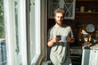 © Marko Geber - Portrait of a young man enjoying morning coffee by the window in cozy kitchen