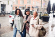 © Davor - Three stylish women walking and laughing together on a city street with coffee