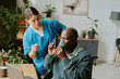 © AnnaStills - Healthcare professional assisting black elderly man with oxygen mask, scene showing interaction and care in well-lit room with plants and medical equipment