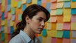 © claudunia - Focused woman in front of a colorful sticky note wall.