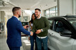 © DusanJelicic - A close-up of a casually dressed couple standing next to a white car, facing us. The salesman in a blue suit, shakes hands with the man while handing him the keys. Everyone looks happy and smiling.