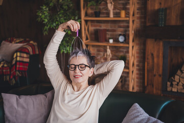 Wall Mural - Charming mature woman enjoying a relaxing day indoors, sitting comfortably on sofa, wearing glasses, smiling peacefully at home