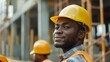© iuricazac - A construction worker in a hard hat and safety vest poses for a photo with his co-worker visible in the background.