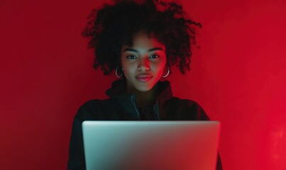 Poster - Young woman with curly hair using laptop, red background, focused expression, modern technology, digital lifestyle
