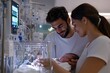 © Milos - A tender moment captured as new parents lovingly gaze at their newborn in a neonatal unit, highlighting the joy and affection that comes with new life.