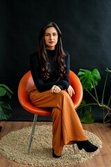 Stylish woman sitting on orange chair indoors