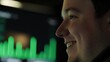 © Sam - Smiling young Caucasian male in profile, focused on data analysis, with vibrant green graph on a screen behind him.