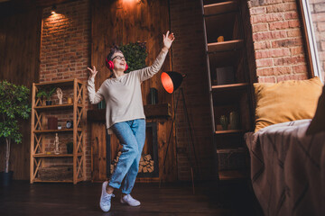 Wall Mural - Elderly woman enjoying music indoors with red headphones, dancing in cozy home setting. Mature female in casual outfit expressing joy