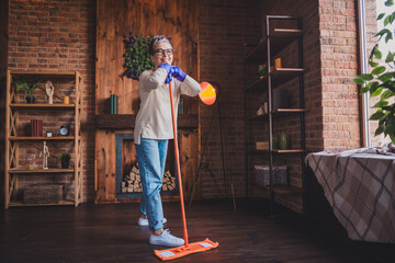 Wall Mural - Charming elderly woman with grey hair enjoying a leisurely day indoors, smiling while mopping the floor in her cozy apartment