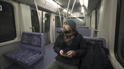 Man traveling on subway train in Hamburg sitting on blue seat and using smartphone wearing winter clothes. Hamburg metro commuter browsing internet on phone while commuting. Hamburger U-Bahn. 