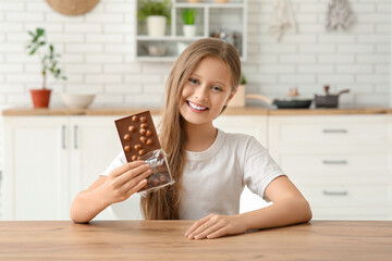 Wall Mural - Cute little happy girl with bar of chocolate in kitchen at home