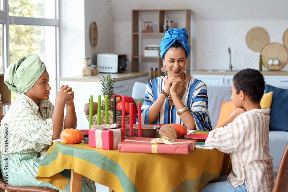 African-American mother with her children praying before dinner at home. Kwanzaa celebration